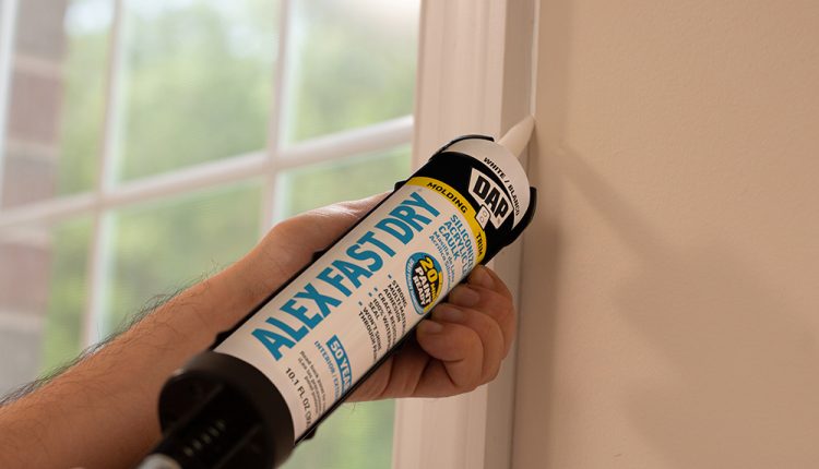 robotnik w kasku nakłada biały silikon wokół okna w domu